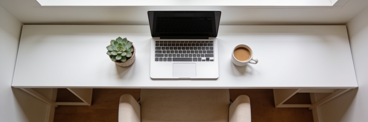 A clean minimal workspace scene viewed from slightly above, a laptop, a small potted succulent, and a cup of coffee on a white desk, soft natural light, wide panoramic crop, lifestyle photography